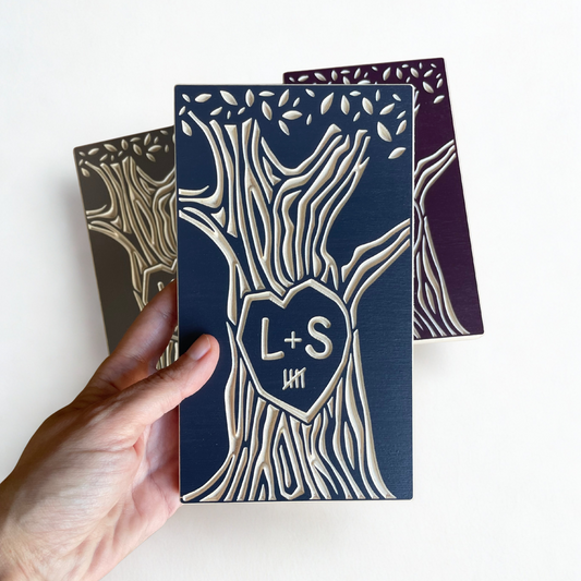 Hand holding a personalized wooden anniversary gift with 'L+S' initials, 5 year marks, and tree design on a white background