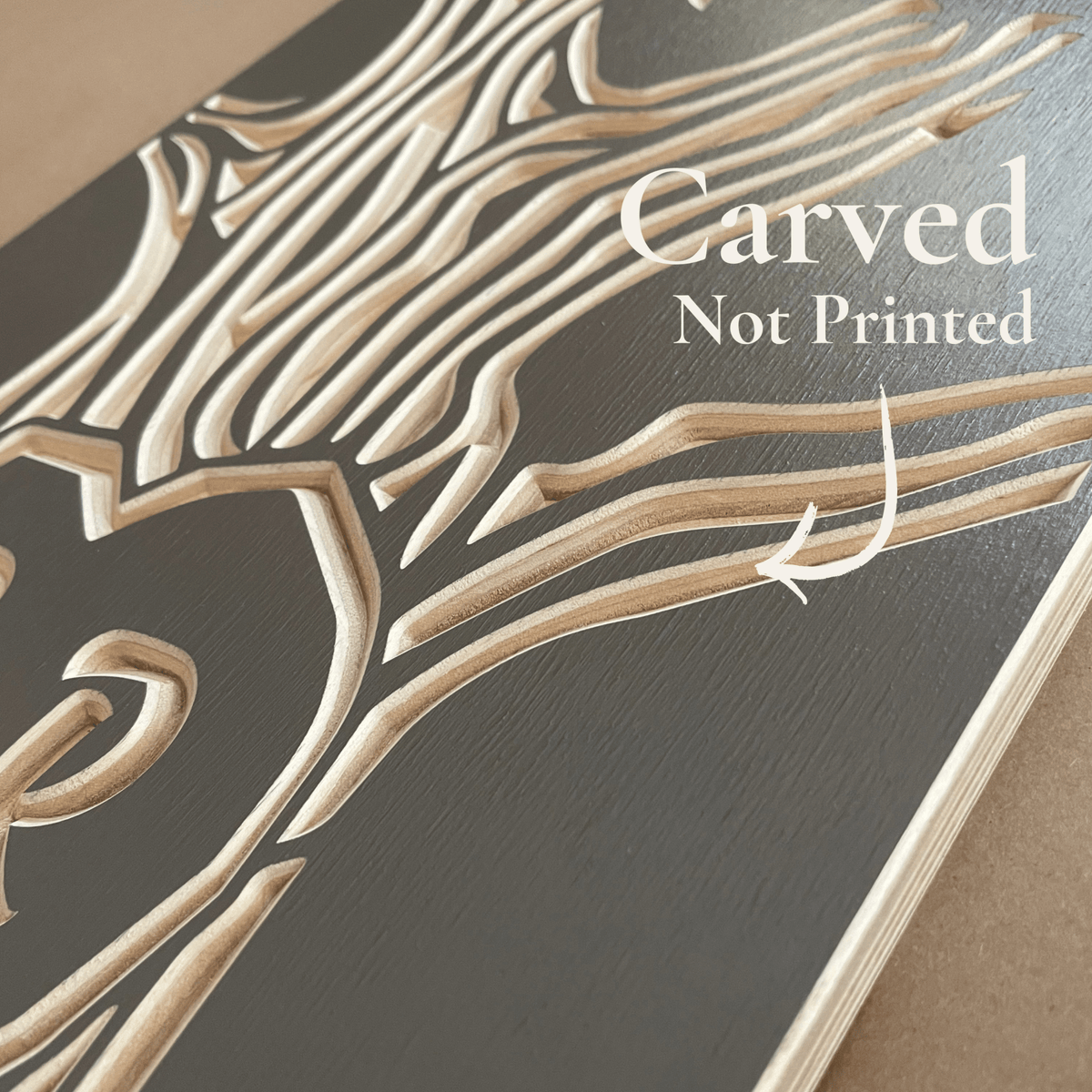 A close-up of a gray wooden board with a  carved tree branch pattern in a light natural wood tone. White text overlay reads 'Carved Not Printed' with a curved arrow pointing to the carved wood texture.