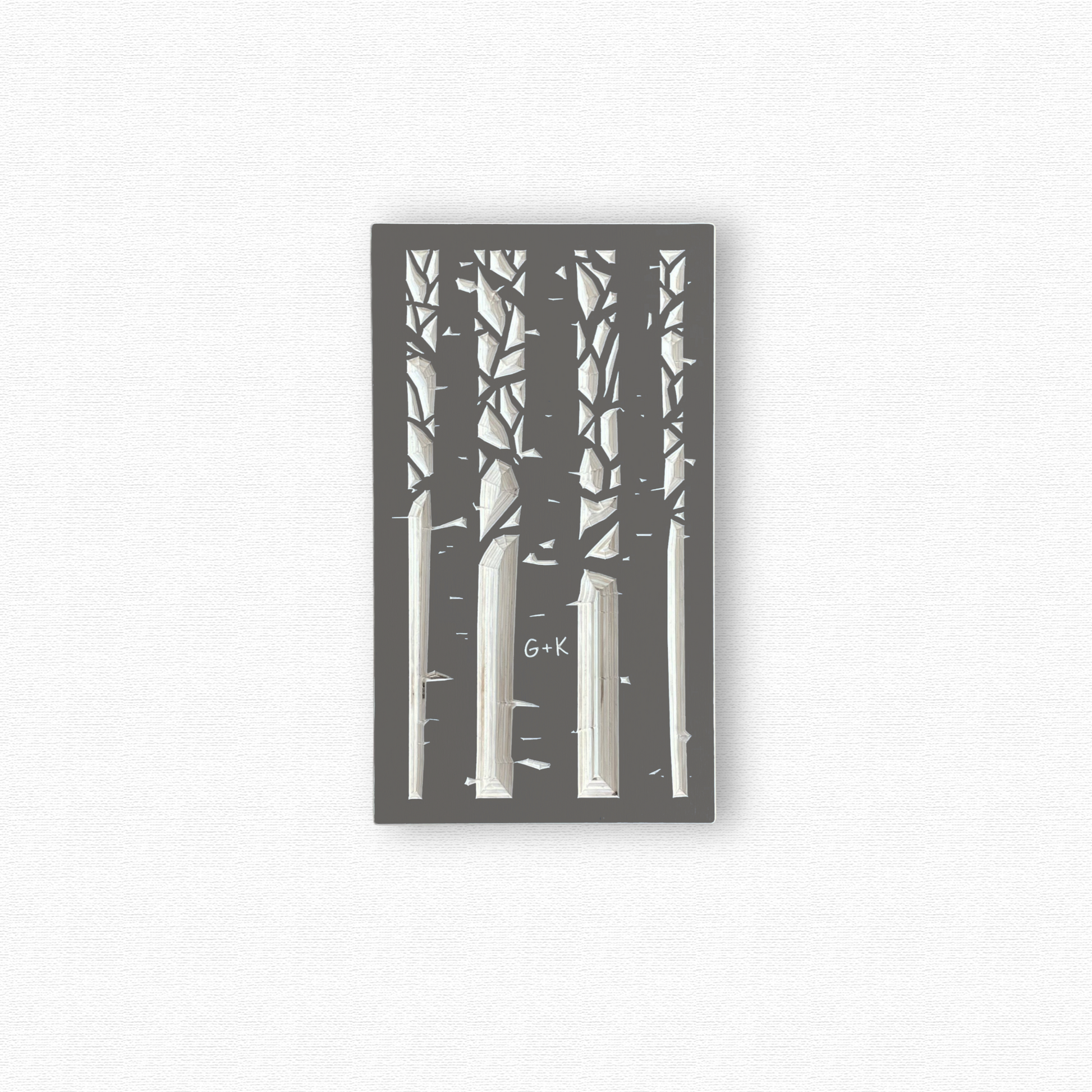 Decorative wooden wall art with black silhouettes of an aspen forest with a couple's initials carved in a trunk. Shown in taupe gray finish on white background.