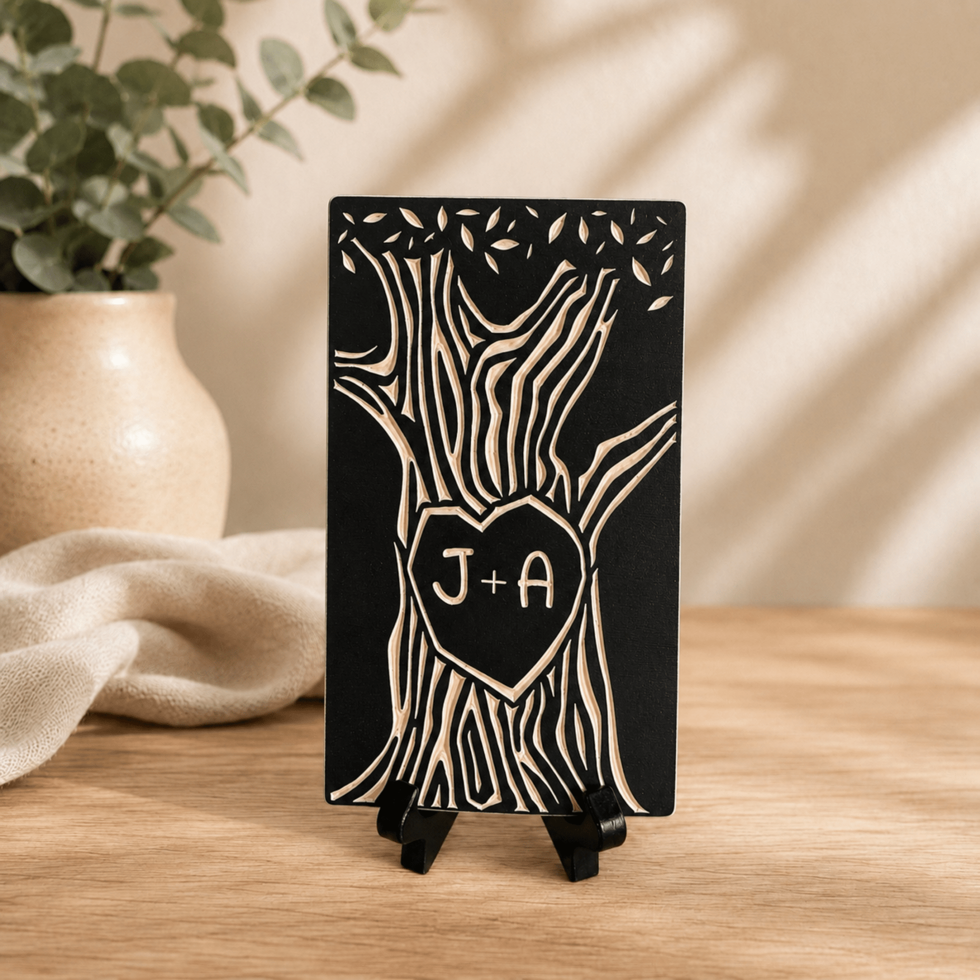 Small carved tree with two initials, shown in black finish on a wooden shelf as an anniversary keepsake. 
