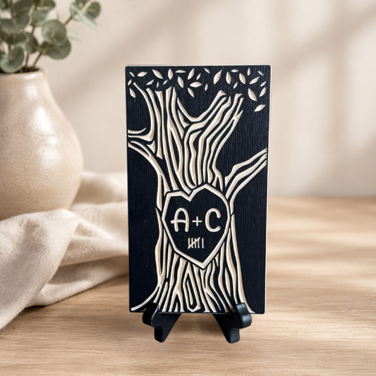 A personalized wooden tree plaque with a heart-shaped center containing the initials 'A+C' and 6 tally marks, displayed on a small black stand on a wooden table.