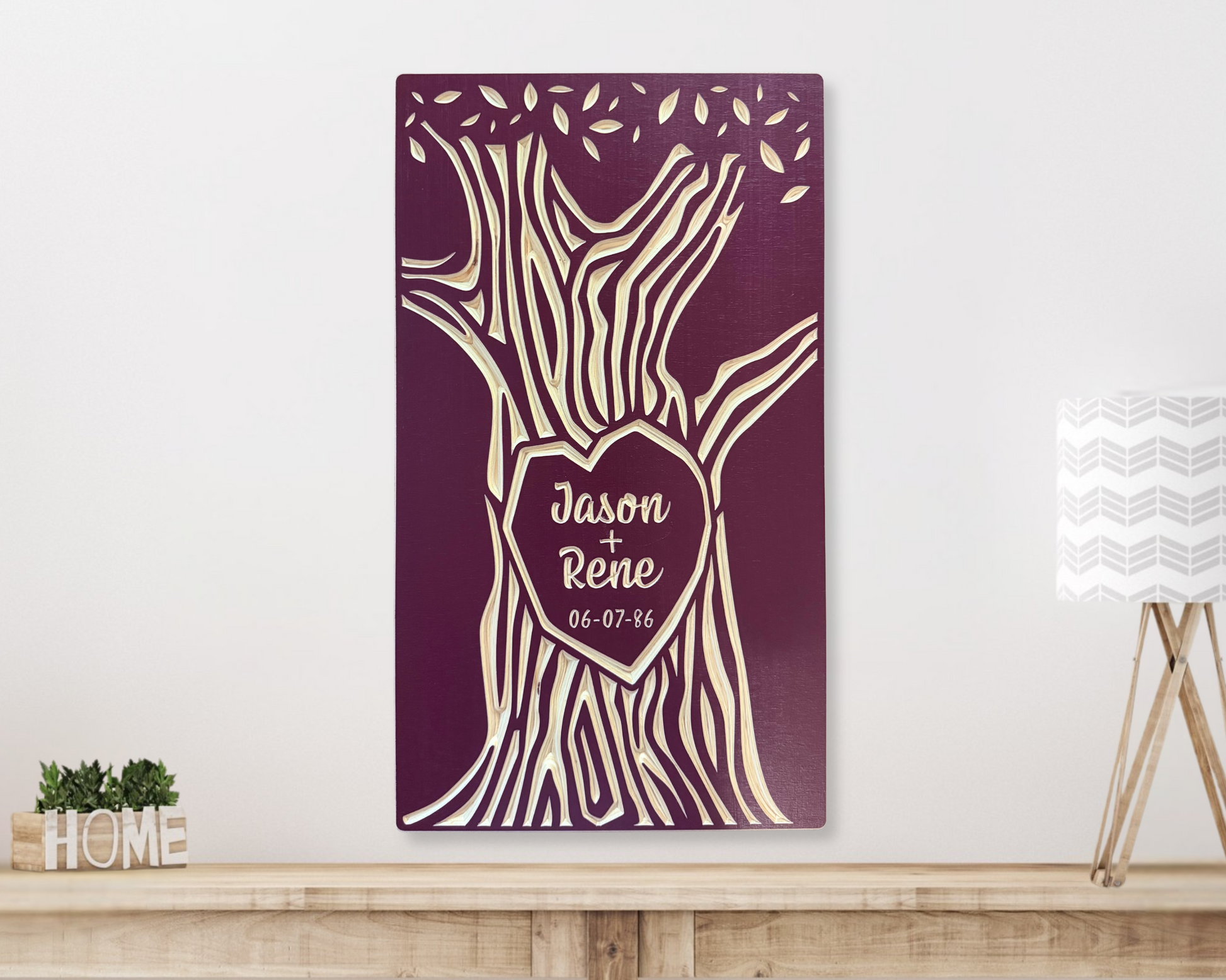 Personalized wood wall art with names carved in tree trunk shown in burgundy finish, hanging on a white wall above a wooden shelf. 