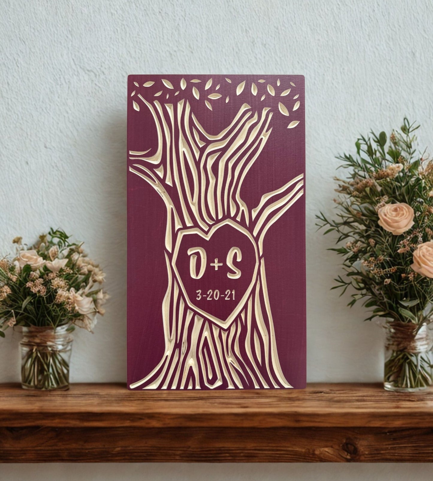 Decorative anniversary wall art with tree design and initials on a wooden shelf with flowers.