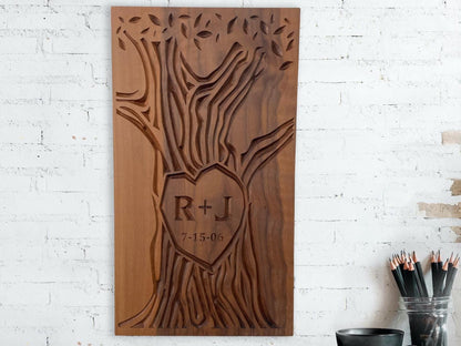 A customizable wall art with initials and wedding date carved into the trunk of a tree design. Artwork is carved on a solid walnut wood panel and shown hanging on a wall above a shelf with accessories on it.