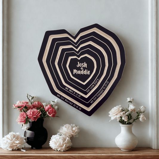 Heart-shaped wall decoration with personalized text on a light gray wall, flanked by two vases with flowers.