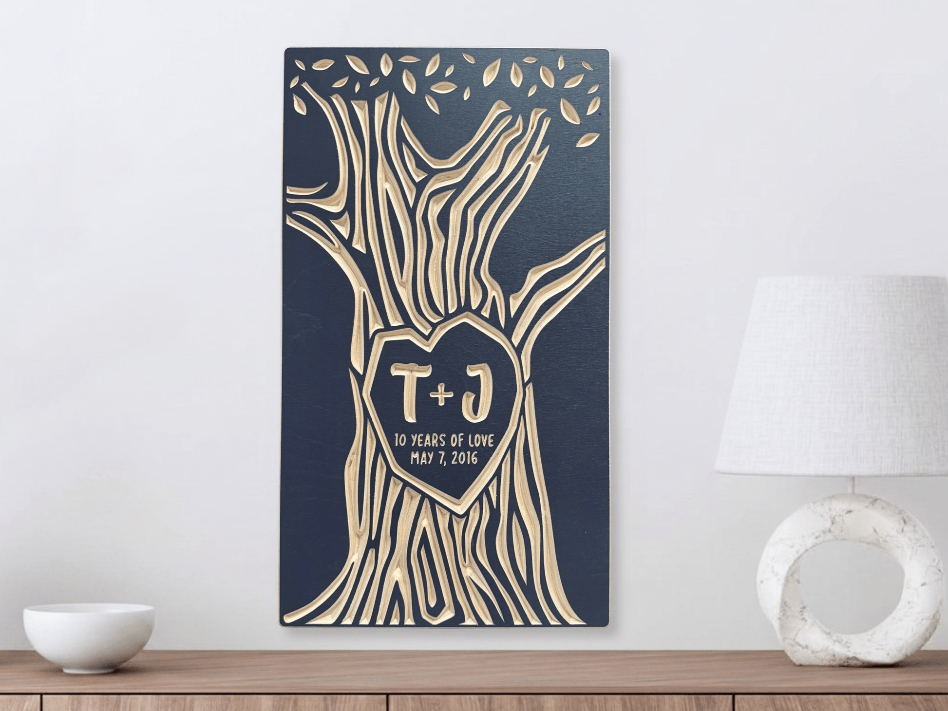 Decorative wall art with tree design and initials on a blue background, placed on a wooden surface.