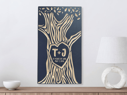 Decorative wall art with tree design and initials on a blue background, placed on a wooden surface.