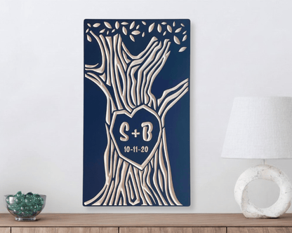 Decorative wall art with tree design and initials on a blue background, placed on a wooden surface with a lamp and decorative bowl.
