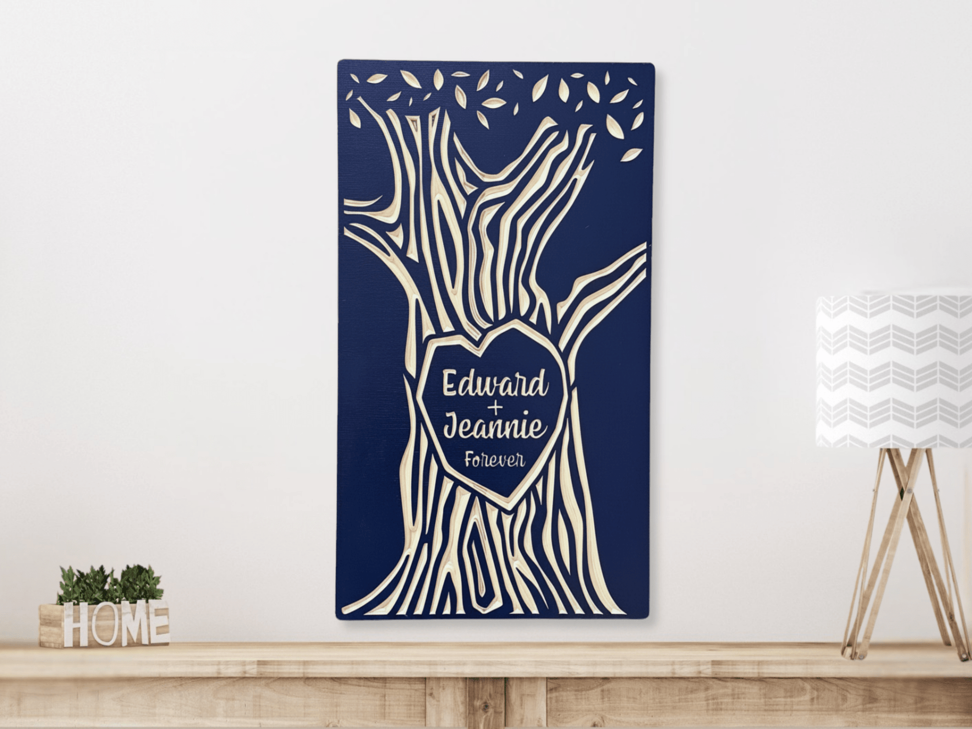 Decorative wall art with tree design and 'Edward + Jeannie Forever' text on a navy blue background, displayed hanging above a shelf.