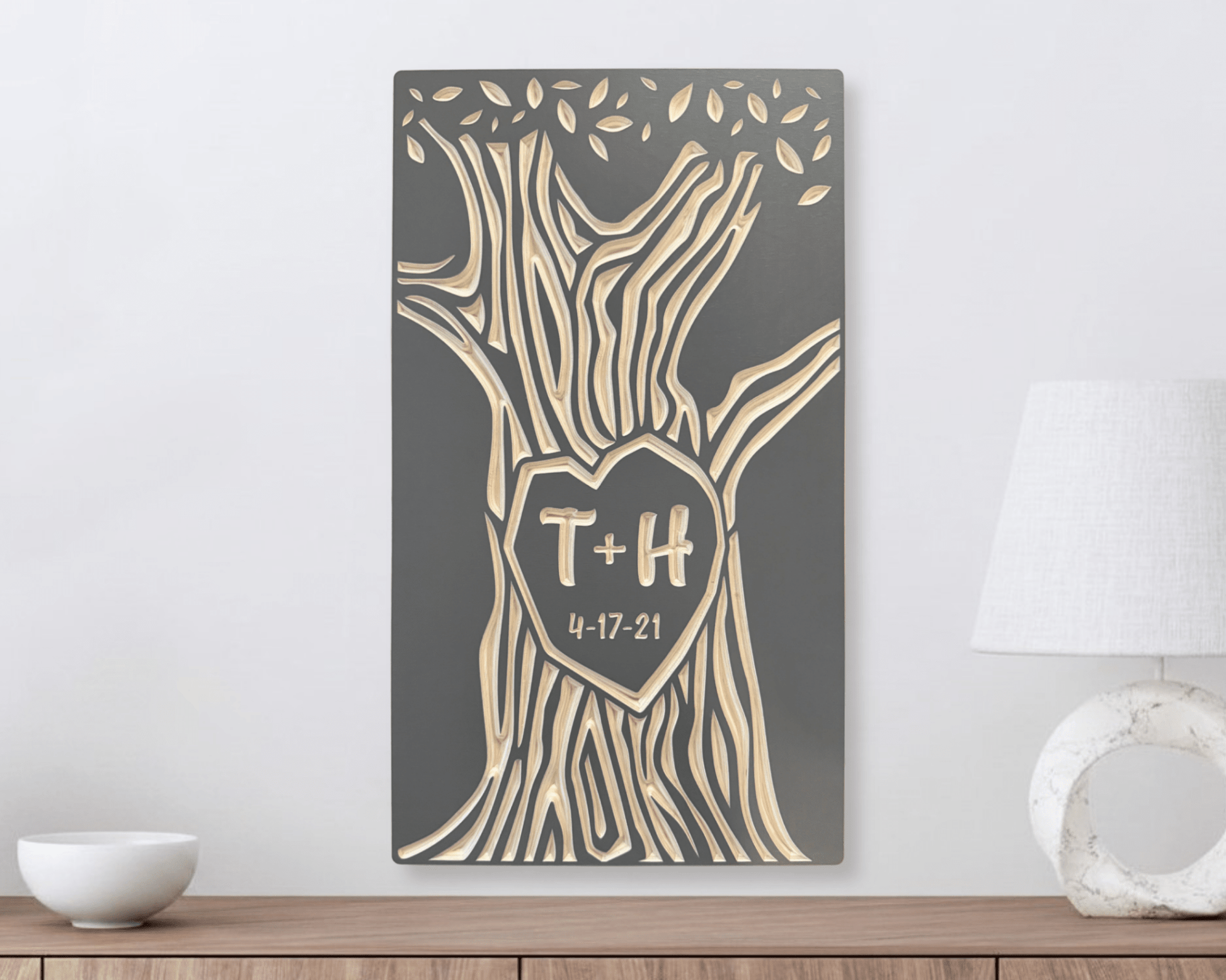 Decorative wall art with tree design and custom initials with anniversary date in taupe color option. Shown hanging on white wall above a wooden shelf.